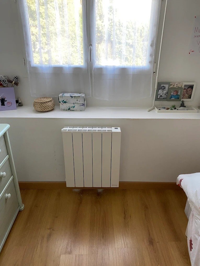 Radiateur électrique mural installé dans une chambre avec sol en parquet et fenêtre en hauteur à Soisy-sous-Montmorency, Val d’Oise, France.
